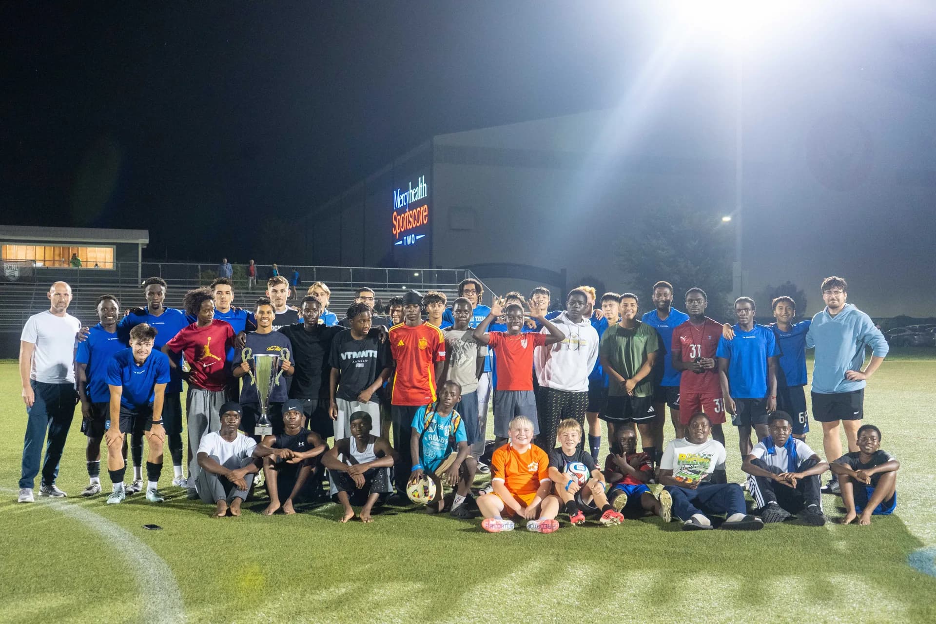 Players, coaches and families with the trophy under the lights at Mercyhealth Sportscore Two